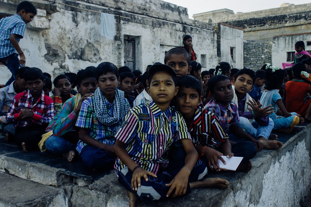 Ethnic barefoot kids in casual clothes sitting on stone floor while studying in local school and looking at camera